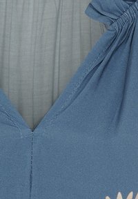 Blåt stof med en glat tekstur, der har en V-udskæring. Indeholder justerbare, rynkede detaljer ved skuldrene.