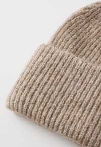 Barna kötött sapka ribbed textúrával, puha gyapjúból vagy hasonló anyagból készült, hajtogatott simlis résszel a megnövelt kényelem érdekében.