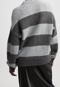 Harmaa ja vaaleanharmaa raidoitettu neulepusero, jossa on ribattu helma ja pyöreä kaula-aukko. Pusero on löysästi istuva ja siinä on teksturoitu kangas.