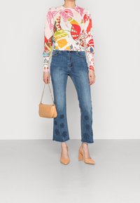 Pestrý květinový svetr s dlouhým rukávem, světle modré džíny s vysokým pasem zdobené vyšívanými květinami, béžová kabelka a odpovídající vysoké podpatky.