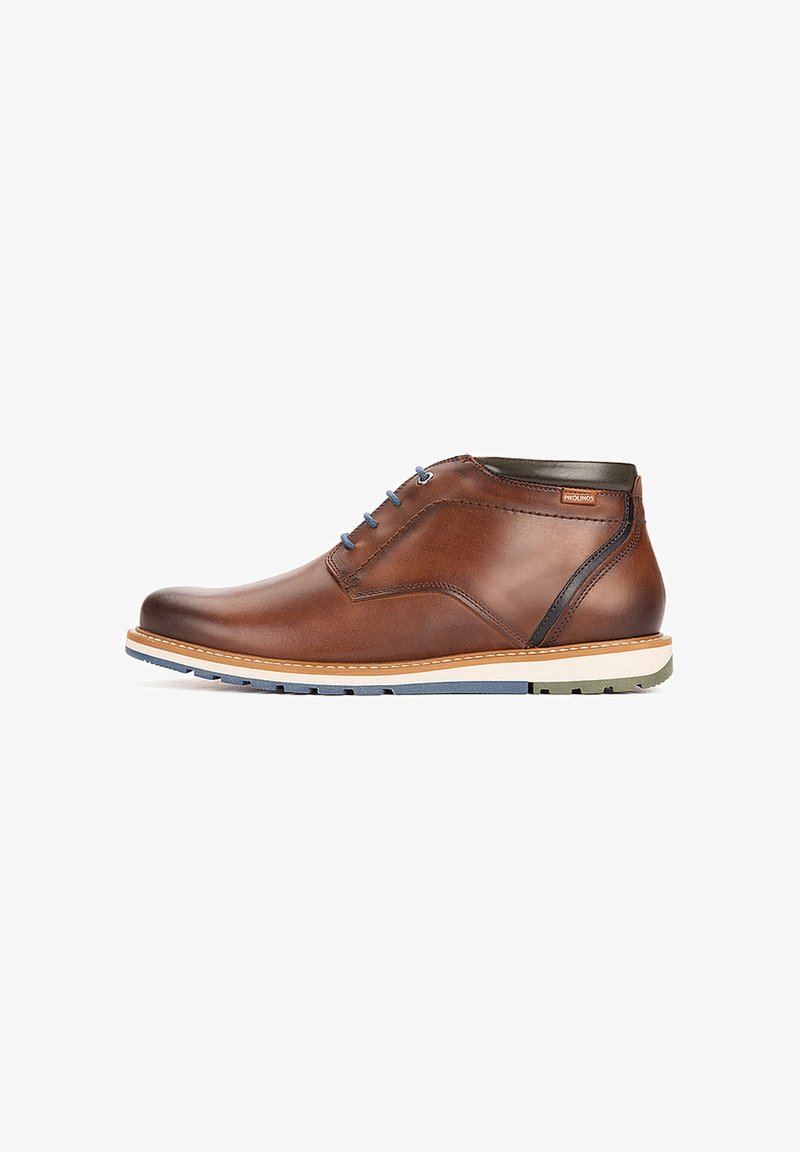 Chaussure montante en cuir marron avec lacets bleus, semelle en caoutchouc blanche et bleue et petite étiquette de marque près du col de la cheville.