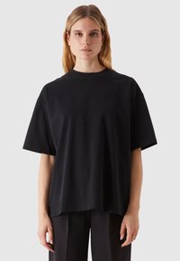 Fekete, oversized póló, kerek nyakkivágással, rövid ujjal, sima pamut anyagból, laza fazonnal, minták nélkül, fekete nadrággal párosítva.