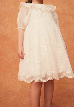 Robe blanche avec manches bouffantes, motifs floraux brodés et ourlet festonné. Confectionnée dans un tissu léger, conçue pour une coupe décontractée.