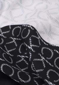 Écharpe noir et blanc présentant un motif noir audacieux de lettres entrelacées sur un fond clair avec un design répétitif subtil.