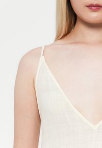 Top body alb fără mâneci, cu decolteu adânc în V și bretele subțiri. Fabricat dintr-un material ușor, texturat, cu o aparență ușor transparentă.