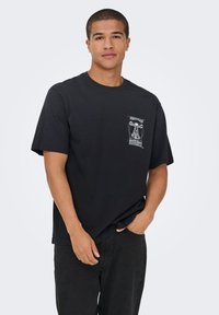 T-shirt preta de algodão com mangas curtas, apresentando uma estampa gráfica branca na área do peito esquerdo e um corte descontraído.