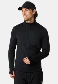 Zwarte fleece jas met ritssluiting aan de voorkant, textuurstof en een getailleerd ontwerp. Voorzien van duimgaten en een borstzak.