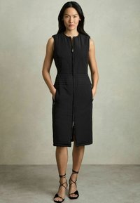 Vestito nero senza maniche con zip frontale, caratterizzato da una texture trapuntata, tasche laterali e un taglio al ginocchio. Abbinato a sandali neri con cinturini.