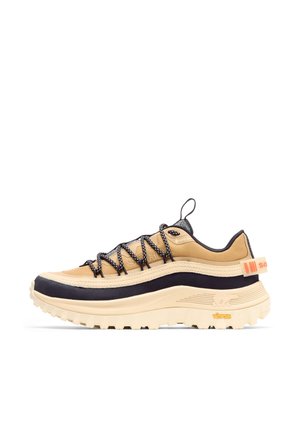 Chaussure de randonnée beige et noire avec semelle Vibram épaisse, lacets noirs et blancs, languette et talon avec languette de traction, et étiquette Gore-Tex sur le côté.