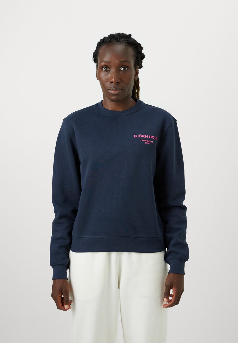 Námořnická modrá mikina vyrobená z bavlněné směsi s žebrovanými manžetami a spodním lemem. Na hrudi se nachází růžový textový logotyp. Design s těsným, kulatým výstřihem.