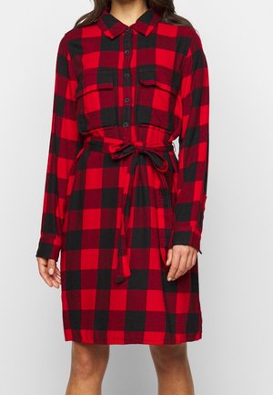 Czerwona i czarna sukienka koszulowa w kratę z zapięciem na guziki z przodu, dwoma kieszeniami na piersi, długimi rękawami oraz paskiem wiązanym w talii. Materiał flanelowy.