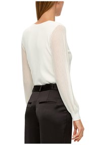 Haut blanc avec manches longues transparentes rayées et encolure ronde, associé à un pantalon noir sur mesure avec poches arrière.