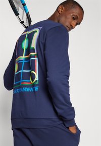 Navy Sweatshirt mit einem bunten geometrischen Grafikdesign auf der Rückseite, aus strukturiertem Material mit Rippbündchen und -saum. Entworfen für Sportbekleidung.