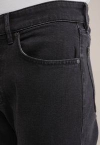 Jeans negri din denim cu o croială clasică, buzunar frontal cu cusături contrastante și o textură netedă. Detaliu de închidere cu un singur nasture vizibil.