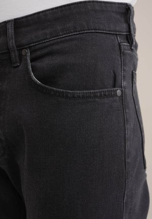 Czarna dżinsowa para spodni o klasycznym kroju, z przednią kieszenią z kontrastowym przeszyciem i gładką fakturą. Widoczny detal z zapięciem na jeden guzik.