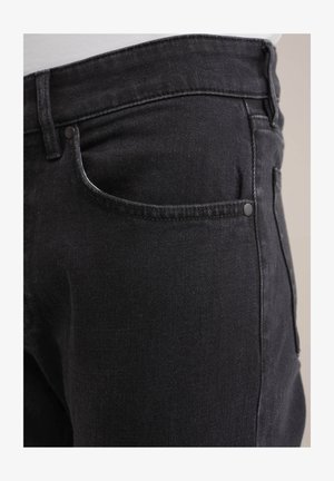 Fekete farmernadrág klasszikus szabással, elülső zseb kontrasztos varrással és sima felülettel. Egy gombos záródás részlet látható.