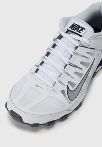 Nike træningssko med en hvid mesh-overdel, grå accenter, fleksibel sål og grøn logo. Har en polstret krave og snørebånd for en sikker pasform.