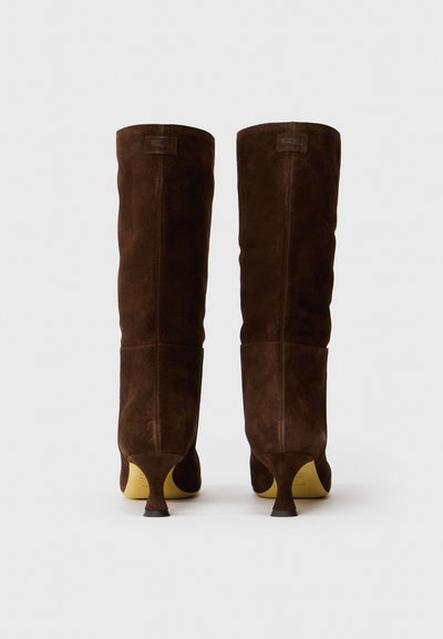 Barna velúr térd fölé érő csizmák, kúpos sarokkal, egyszerű varrási részletekkel. Simább textúrájúak és minimalista stílusúak.