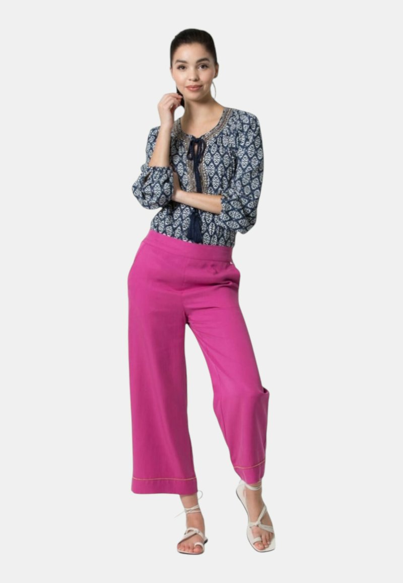 Blusa a fantasia navy con maniche a tre quarti e pantaloni cropped ampi rosa. Sandali bianchi, tessuto leggero e accenti blu e oro.