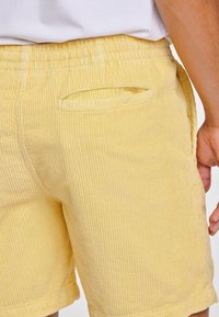 Gula kordflättade shorts med vertikal ribbad textur, midja med elastisk resår och en sidoficka. Sömmen är avslutad med en ren kant.