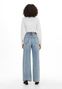 Vit kort denimjacka i kombination med ljusblå vida jeans. Jackan har fransade kanter och detaljerad sömnad. Svarta klackskor med blockklack.