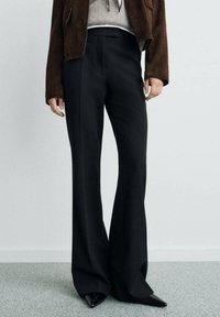 Pantaloni neri a palazzo con una vestibilità su misura, tessuto liscio e vita alta. Abbinati a una giacca in suede marrone e scarpe a punta.