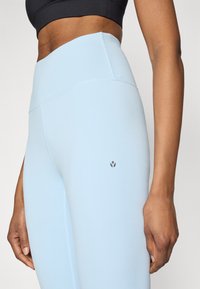 Hele sinise värviga kõrge vöökohaga retuusid, mis on valmistatud venivast materjalist, omavad siledat tekstuuri ja väikest logo detaili reiel.