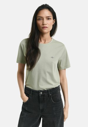 Hellgrünes Baumwoll-T-Shirt mit Rundhalsausschnitt, kurzen Ärmeln und einem kleinen gestickten Logo auf der Brust, kombiniert mit hochtaillierten schwarzen Jeans.