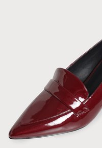 Mocassin en cuir rouge foncé brillant à bout pointu, avec une large bride sur le dessus et une doublure intérieure noire.