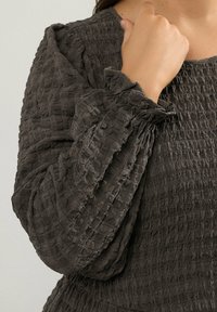 Mörkgrå texturerad blus med skrynkligt tyg, med lös passform och samlade ärmslut för extra detalj.