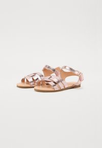 Metalliska roséguld sandaler med flera horisontella remmar, en bakre ankelsrem med spänne och en platt, beige sula.