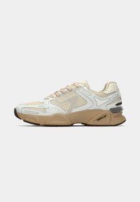 White and beige athletic shoe with a textured mesh design, featuring rubber sole, padded collar, and contrasting logo accents.