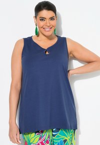 Top senza maniche di colore blu navy con dettaglio a chiave sullo scollo, realizzato in morbido tessuto, abbinato a pantaloni a fantasia vivace.