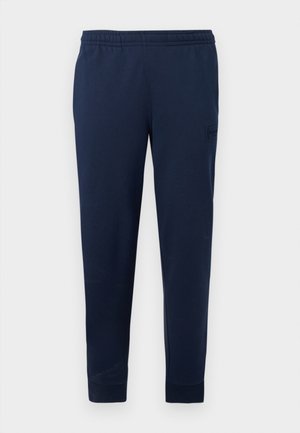 Pantalon de jogging bleu marine avec taille élastique et poignets aux chevilles, arborant un logo discret en patch sur la cuisse supérieure.