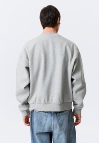 Grauer Pullover mit rundem Ausschnitt. Verfügt über gerippte Bündchen und Saum, weichen Baumwollmischstoff und eine lockere Passform. Rückansicht gezeigt.