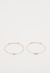 Gold chain bracelets with delicate links; one features a circular, embellished charm while the other has an oval link with small accents.