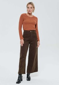 Haut henley à manches longues en rouille avec trois boutons, associé à un pantalon en velours côtelé marron taille haute et large, et des bottes noires à talons.