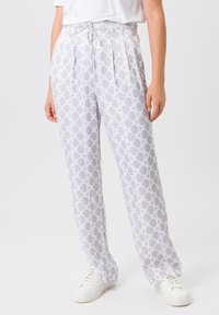 White patterned trousers featuring a gray circular design, pleated front detail, and a high waist. Paired with white sneakers.