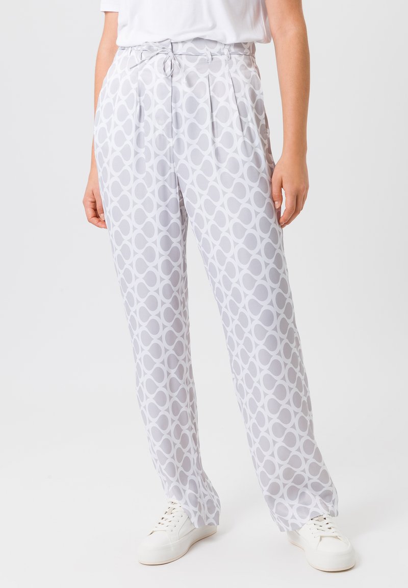 White patterned trousers featuring a gray circular design, pleated front detail, and a high waist. Paired with white sneakers.