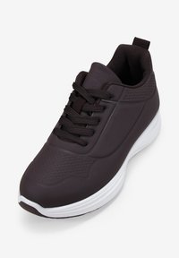 Black athletic shoe with textured upper, round toe, and white sole. Features laces and a pull tab at the back. Perforated detailing present.