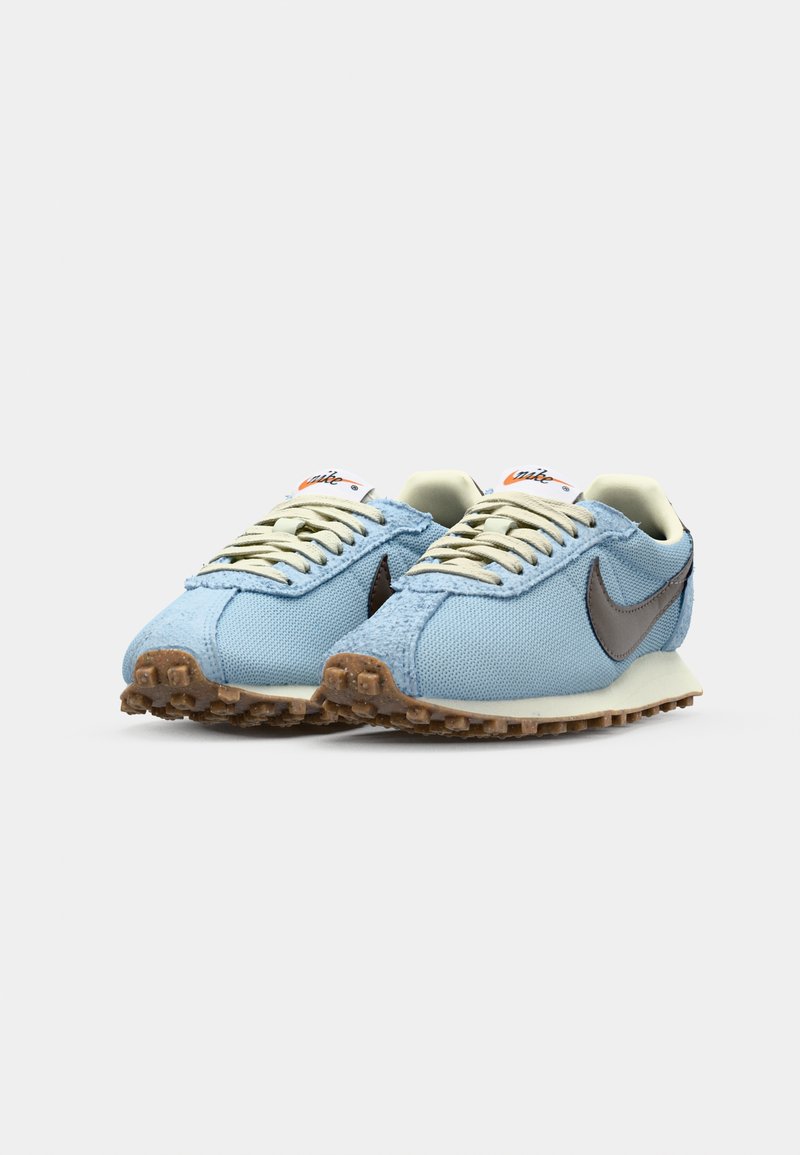 Jasnoniebieskie sneakersy z teksturowanej tkaniny, brązowymi akcentami i beżowymi sznurówkami. Posiadają gumową podeszwę z charakterystycznym wzorem przyczepności.