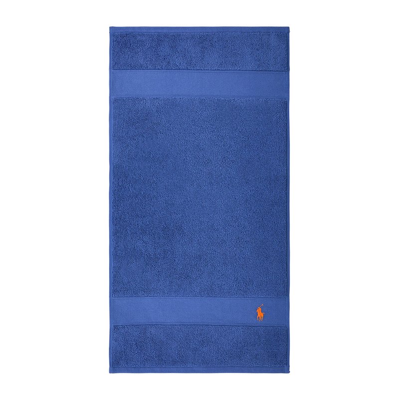 Μπλε βαμβακερή πετσέτα με υφή και ομαλή λωρίδα σ το πάνω μέρος. Διαθέτει πορτοκαλί λογότυπο στην κάτω γωνία.