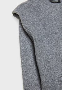 Šedý top s krátkými rukávy vyrobený z měkké, strukturované látky; má kulatý výstřih a mírně polstrované ramenní detaily.