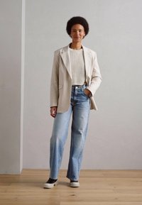 Vaaleanbeige bleiseri kermaisella ribbipuserolla, yhdistettynä vaaleansinisiin leveälahkeisiin farkkuihin ja mustiin slip-on -kengiin. Minimalistinen muotoilu ja materiaalit.