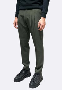 Pantaloni plissettati verde oliva con design a gamba dritta, realizzati in tessuto liscio, abbinati a scarpe nere stringate con suole robuste.
