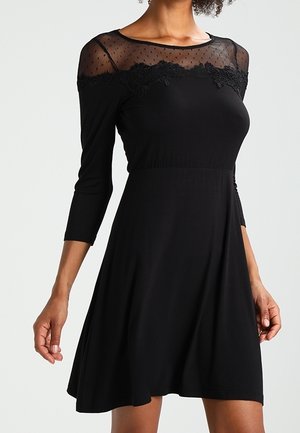 Black dress featuring a sheer, dotted yoke with lace accents, three-quarter sleeves, and a flared skirt design. Soft stretch fabric.