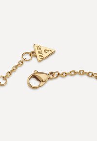 Gold metal chain with a triangular charm labeled "GUESS" and a lobster clasp, featuring a smooth surface and shiny finish.