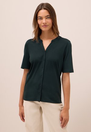 Chemisette à manches courtes de couleur vert foncé avec un col à enfiler et un tissu lisse et léger. Design uni sans motifs ni accents.