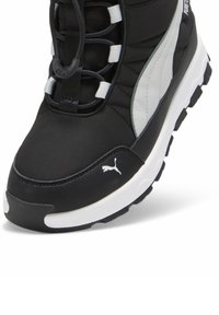 Zapatilla deportiva negra y gris con parte superior acolchada, tejido texturizado, cordones elásticos y un logo blanco en el costado. Suela de goma plana.