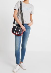 Camiseta gris de algodón con el logo de "Tommy Hilfiger", jeans ajustados azules, zapatillas blancas y un pequeño bolso cruzado de color marino con acentos rojos.